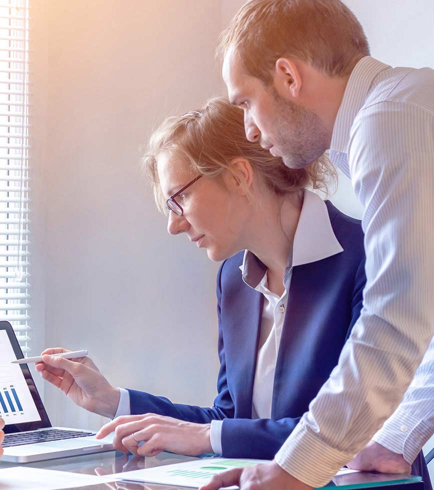 businesswoman pointing to computer with tablet pen with businessman leaning over her shoulder