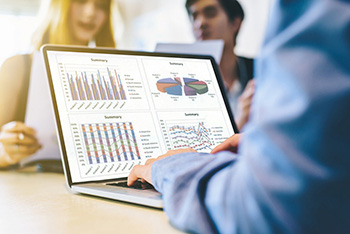 man typing on computer with charts and graphs with two people on computers in the background