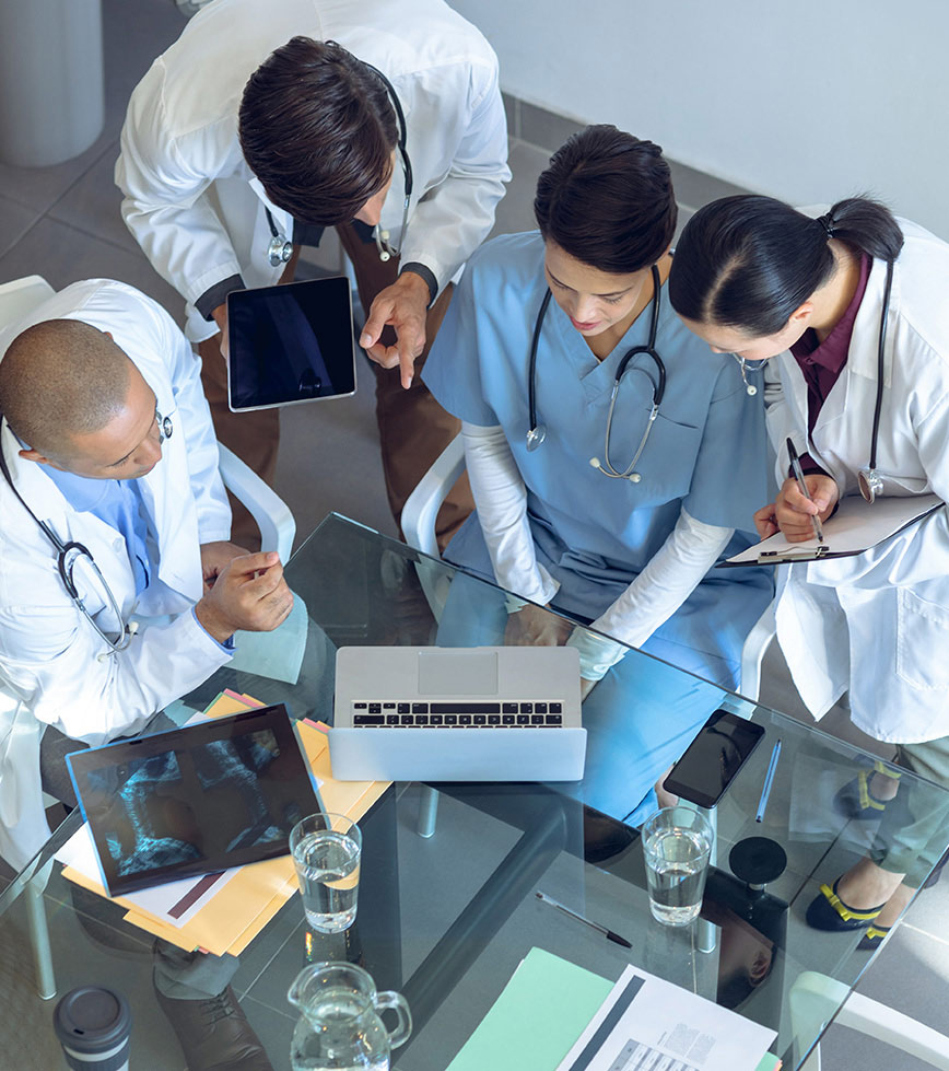 4 medical personnel looking at computer on glass table with water cups and x ray sheet on it