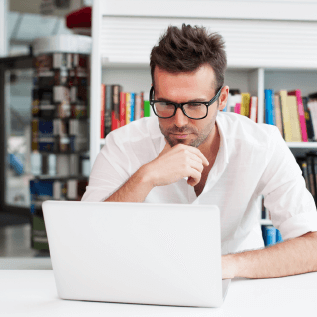 Seated man wearing black glasses in office looking at computer