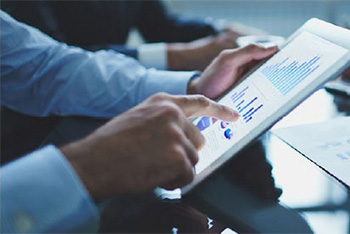 businessman pointing to tablet with charts on it with two business people in the background