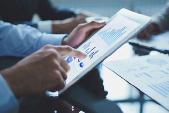 businessman pointing to tablet with charts on it with two business people in the background