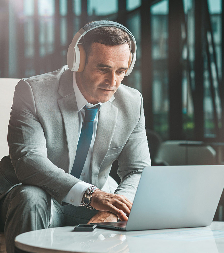 Man in grey suit with white over the head headphones on working on computer
