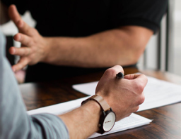 Man's hand with watch holding pen over paper with other person holding hand out